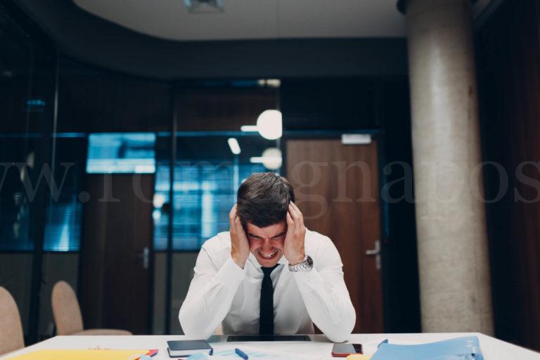 Sad young businessman sit and hold head with his hands at office table. Business people headache in crisis and depression after covid-19 pandemia concept