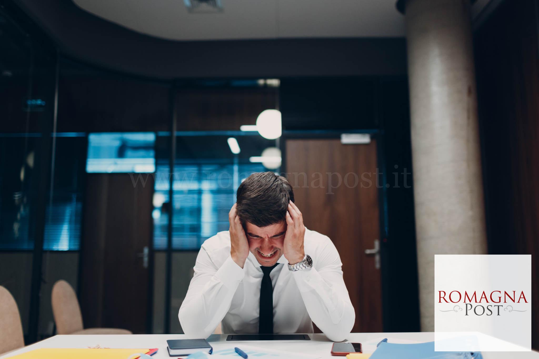 Sad young businessman sit and hold head with his hands at office table. Business people headache in crisis and depression after covid-19 pandemia concept